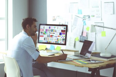 İnternette çalışırken bilgisayarın ve dizüstü bilgisayarın önünde grafik stüdyosunda oturan genç tasarımcının portresi.