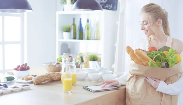 Giovane donna che tiene borsa della spesa con verdure. In piedi in cucina — Foto Stock