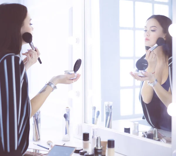 Schönes Mädchen, das in den Spiegel schaut und Kosmetik mit einem großen Pinsel anwendet — Stockfoto