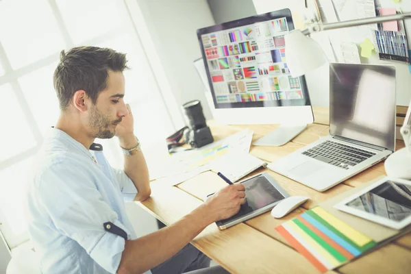 Porträt eines jungen Designers, der im Grafikstudio vor Laptop und Computer sitzt, während er online arbeitet. — Stockfoto