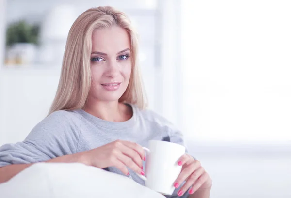 Portrett av en ung kvinne som sitter på sofaen med en kopp kaffe – stockfoto