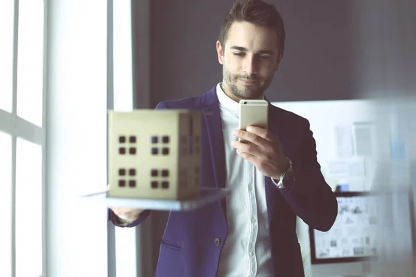 Homme d'affaires tenant maison miniature à portée de main debout dans le bureau . — Photo