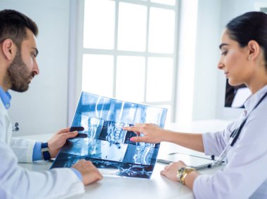 İki doktor röntgen görüntülerini inceliyor, parlak ofiste danışmanlık yapıyorlar.