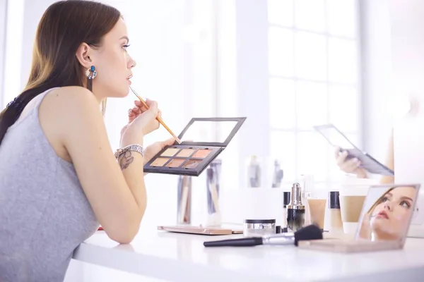 Mujer morena aplicando maquillaje para una cita nocturna frente a un espejo —  Fotos de Stock