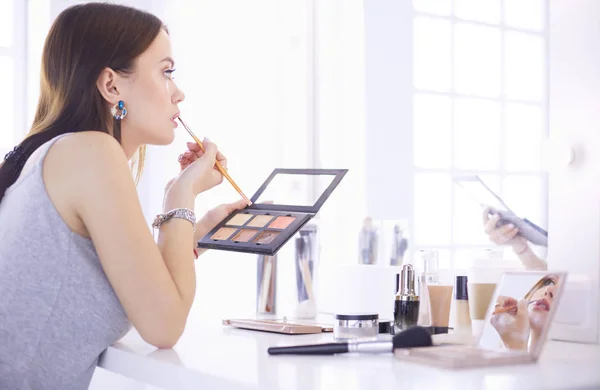 Mujer morena aplicando maquillaje para una cita nocturna frente a un espejo — Foto de Stock