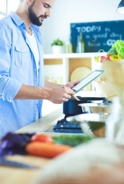 Dijital tablet ve yemek pişirme tarifine uyan bir adam evdeki mutfakta lezzetli ve sağlıklı yemekler pişiriyor.
