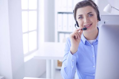 Ofisinde kulaklık takmış, telefon operatörü olarak çalışan ciddi ve güzel bir genç kadın.