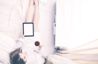 Sabahları yatakta otururken tablet kullanan ve kahve içen kadın portresi