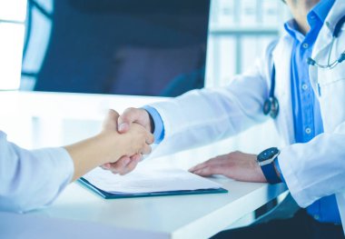 Yakışıklı doktor genç bayan hastasıyla konuşuyor ve ofisinde otururken notlar alıyor.