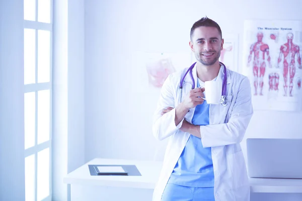 Retrato médico masculino joven y confiado de pie en el consultorio médico. — Foto de Stock