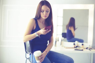 Kafede kahve içip cep telefonuyla konuşan genç bir kadın.