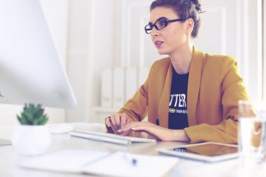 Ofis masasında çalışan ve dizüstü bilgisayarla yazan kendine güvenen genç bir iş kadını.