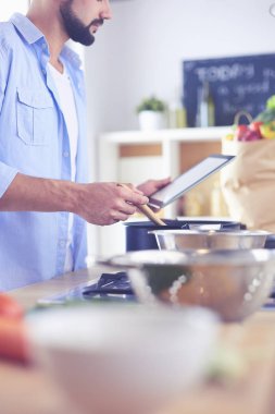 Dijital tablet ve yemek pişirme tarifine uyan bir adam evdeki mutfakta lezzetli ve sağlıklı yemekler pişiriyor.