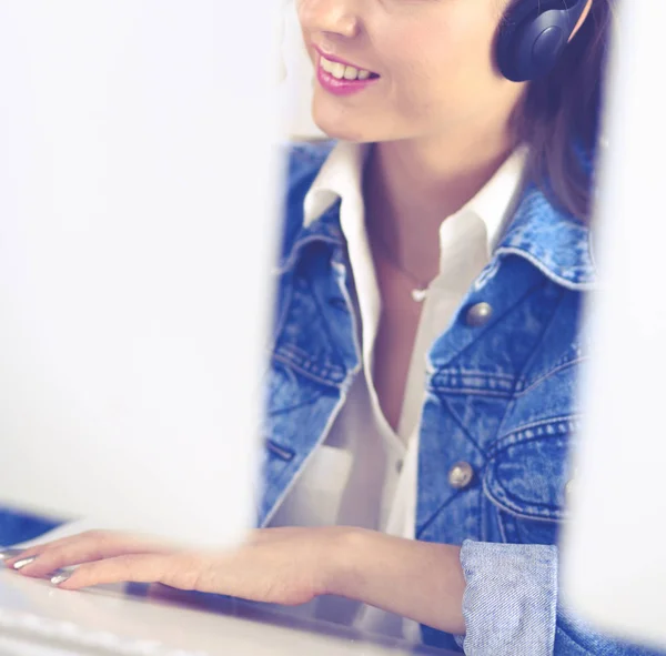 Feliz encantadora joven sentada y trabajando con el ordenador portátil con auriculares en la oficina —  Fotos de Stock