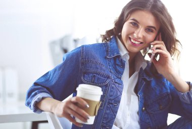 Kafede kahve içip cep telefonuyla konuşan genç bir kadın.