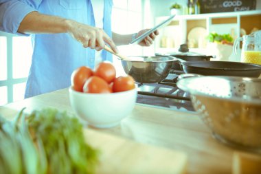 Dijital tablet ve yemek pişirme tarifine uyan bir adam evdeki mutfakta lezzetli ve sağlıklı yemekler pişiriyor.