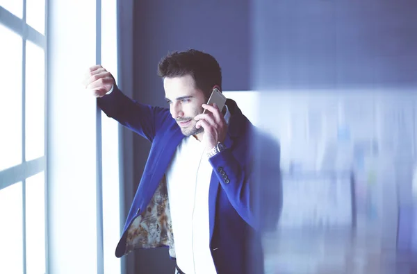 Homem de negócios de terno falando ao telefone e olhando para longe perto da janela . — Fotografia de Stock