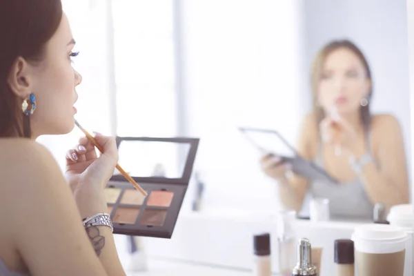 Brunette vrouw solliciteren make-up voor een avond date voor een spiegel — Stockfoto