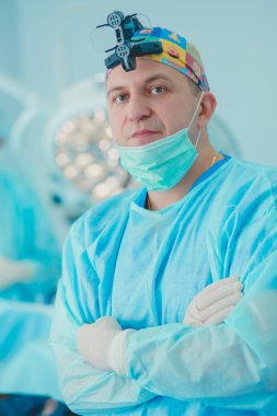 Ameliyat odasında arka planda erkek cerrah var.