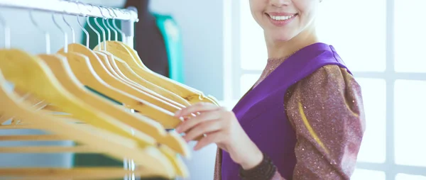 Beautiful young stylist near rack with hangers