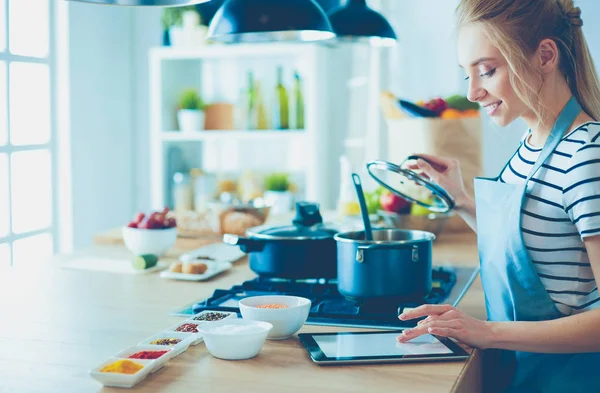 Mujer joven usando una tableta para cocinar en su cocina — Foto de Stock