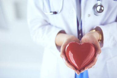 Steteskop tutan, kalbi hafif arka planda olan kadın bir doktor.