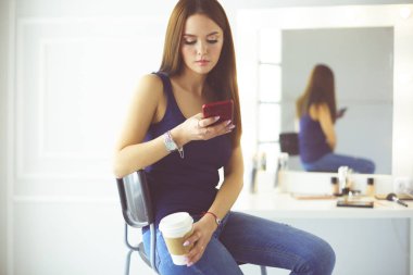 Kafede kahve içip cep telefonuyla konuşan genç bir kadın.