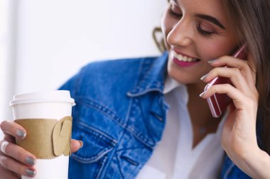 Kafede kahve içip cep telefonuyla konuşan genç bir kadın.