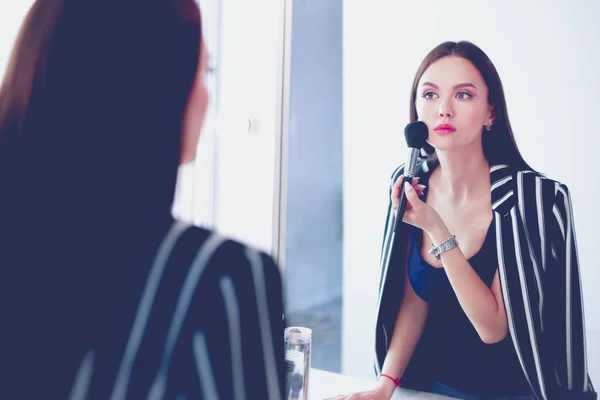 Mujer de belleza aplicando maquillaje. Hermosa chica mirando en el espejo y la aplicación de cosméticos con un cepillo grande —  Fotos de Stock