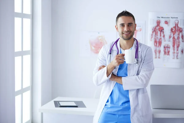 Jonge en zelfverzekerde mannelijke arts portret staan in medisch kantoor. — Stockfoto