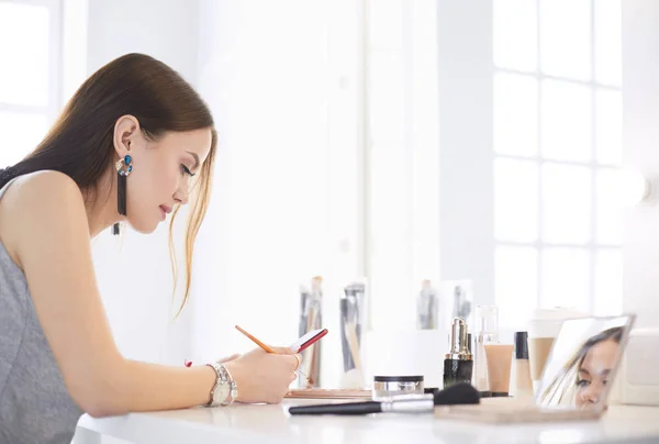 化粧台に座って化粧をする美しい若い女性 — ストック写真