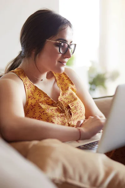 Young woman sitting on couch working on laptop computer at home