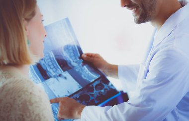 Yakışıklı doktor genç bayan hastasıyla konuşuyor ve ofisinde otururken notlar alıyor.