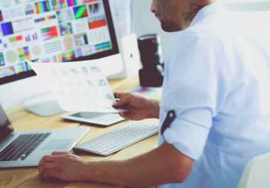 İnternette çalışırken bilgisayarın ve dizüstü bilgisayarın önünde grafik stüdyosunda oturan genç tasarımcının portresi.