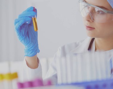 Bir kadın tıbbi veya bilimsel araştırmacı ya da kadın doktor laboratuarda bir test tüpü dolusu temiz çözeltiye bakıyor.