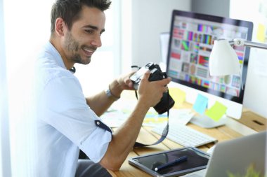 İnternette çalışırken bilgisayarın ve dizüstü bilgisayarın önünde grafik stüdyosunda oturan genç tasarımcının portresi.