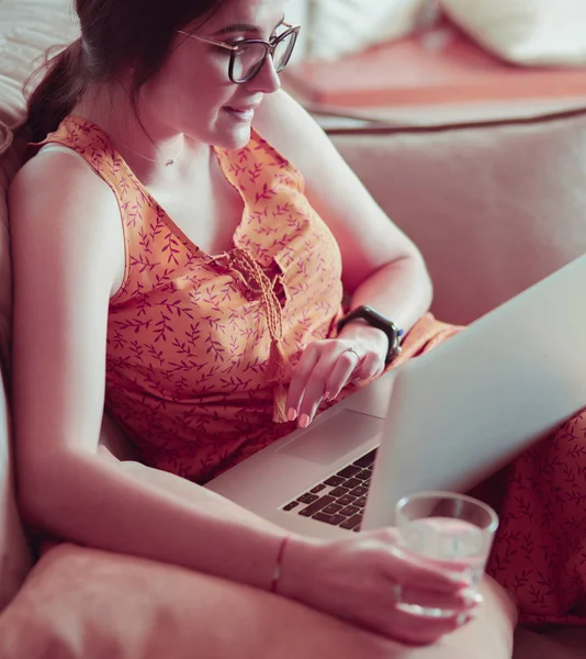 Young woman sitting on couch working on laptop computer at home