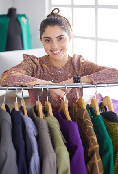 Bonito jovem estilista perto de rack com cabides — Fotografia de Stock