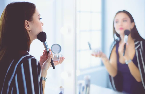 Красива жінка наносить макіяж. Красива дівчина дивиться у дзеркало і наносить косметику великою щіткою — стокове фото