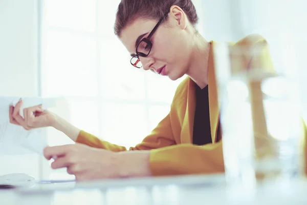 Mooie jonge zakenvrouw doet wat papierwerk terwijl zitten aan kantoor bureau in de voorkant van laptop — Stockfoto