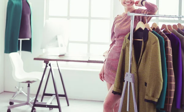 Bonito jovem estilista perto de rack com cabides — Fotografia de Stock