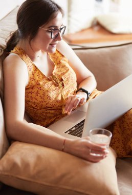 Evde dizüstü bilgisayar üzerinde çalışan kanepede oturan genç kadın