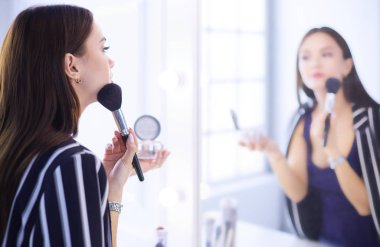 Güzellik kadını makyaj uygulamak. Aynaya bakıyorum ve büyük bir fırça ile kozmetik uygulama güzel kız