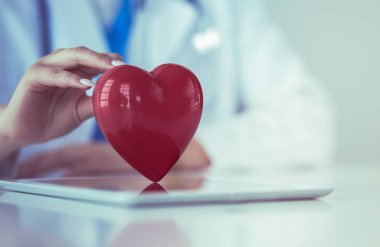 Steteskop tutan, kalbi hafif arka planda olan kadın bir doktor.