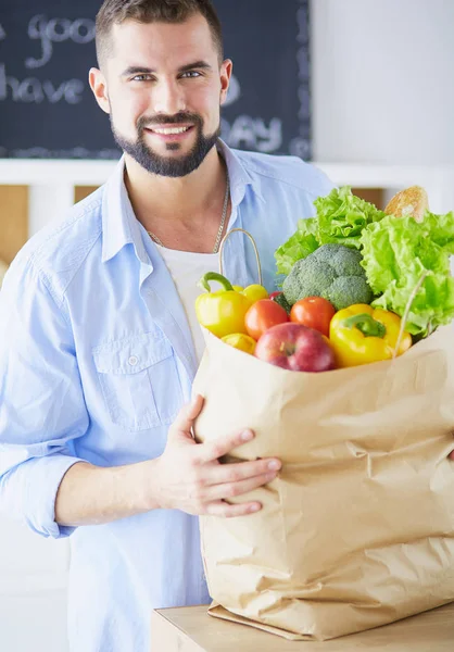 Man holding paper bag full of groceries on the kitchen background. Shopping and healthy food concept