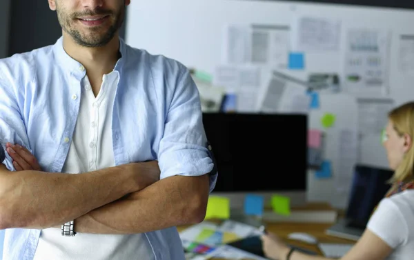 Porträt eines jungen Designers vor Laptop und Computer während der Arbeit. Assistentin bedient ihr Handy im Hintergrund. — Stockfoto