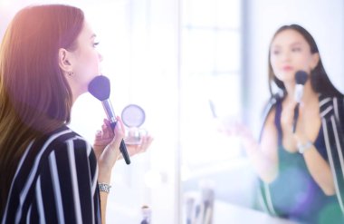 Güzellik kadını makyaj uygulamak. Aynaya bakıyorum ve büyük bir fırça ile kozmetik uygulama güzel kız