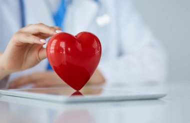 Steteskop tutan, kalbi hafif arka planda olan kadın bir doktor.