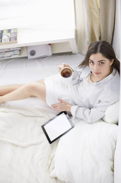 Portrét ženy pomocí tablet a pití kávy při ranním posezení na posteli — Stock fotografie
