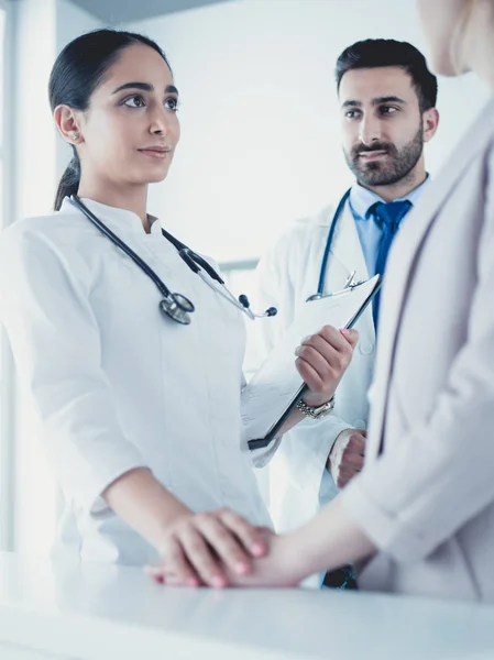 Médico bonito está conversando com jovem paciente do sexo feminino e fazendo anotações enquanto está sentado em seu escritório — Fotografia de Stock